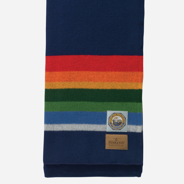 A folded navy blue wool scarf with horizontal rainbow stripes in red, orange, yellow, green, blue, and white, featuring a Pendleton brand patch and a circular mountain emblem.