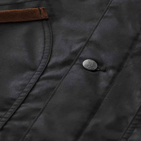 Close-up of a dark charcoal gray jacket or coat fabric with a brown leather trim detail and a silver metal snap button.