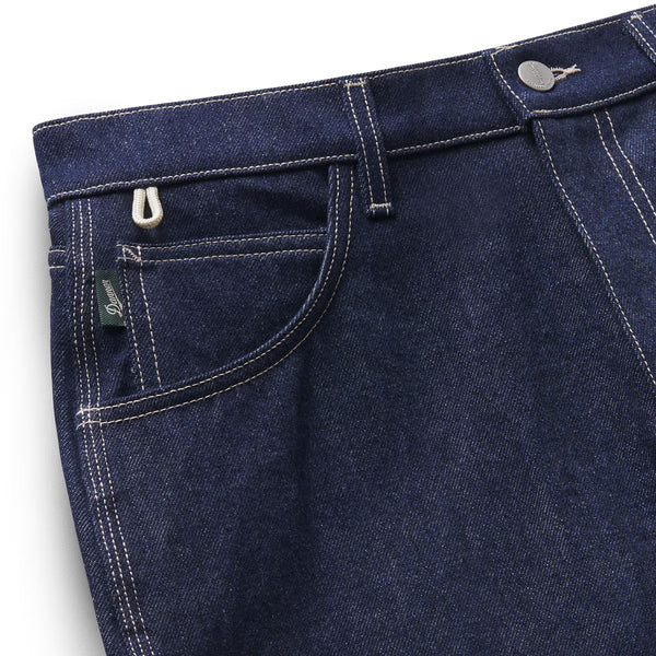 Close-up of dark indigo denim jeans showing the back pocket with white contrast stitching, a silver metal hook-and-loop closure, and a small green Levi's tag.