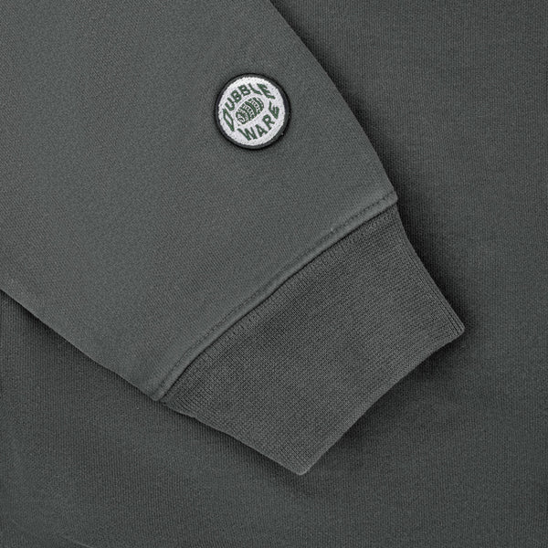 Close-up of a dark gray sweatshirt sleeve with a ribbed cuff and a circular white and black 'Tubble War' patch on the upper arm.