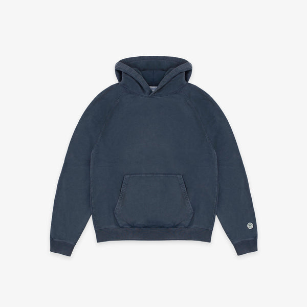 A dark navy blue pullover hoodie with a kangaroo pocket and a small circular white logo on the left sleeve cuff, displayed against a clean off-white background.