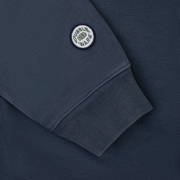 Close-up of a navy blue sweatshirt sleeve with a ribbed cuff and a circular embroidered patch reading 'TUBBLE WAR' on the upper sleeve.