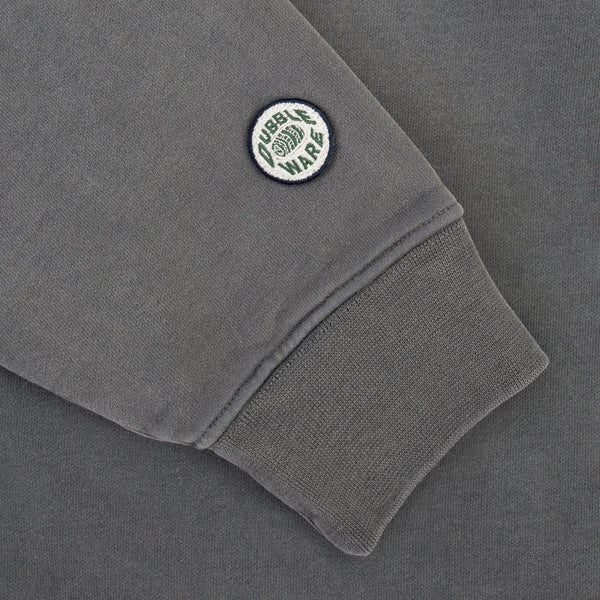 Close-up of a dark gray sweatshirt sleeve featuring a ribbed cuff and a circular embroidered patch that reads 'CUBIK WARS' with a green globe logo.