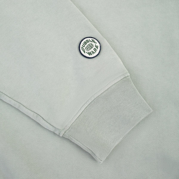 Close-up of a light gray sweatshirt sleeve with a ribbed cuff and a circular embroidered patch reading 'FUEL BURN WARS' on the upper cuff.