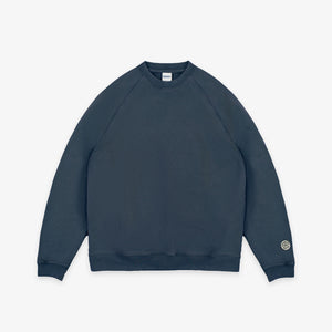 Dubbleware - Dubbleware Vintage Dye Sweatshirt - Washed Navy - A dark slate blue crewneck sweatshirt with raglan sleeves, shown flat against a light gray background. A small circular logo is printed on the left sleeve cuff. - Main Front View