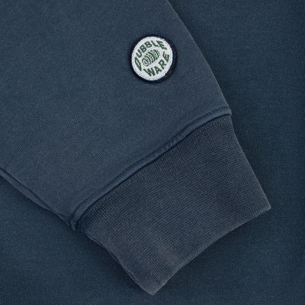 Close-up of a dark slate blue sweatshirt sleeve featuring a circular embroidered 'Dubble Wars' patch on the cuff.