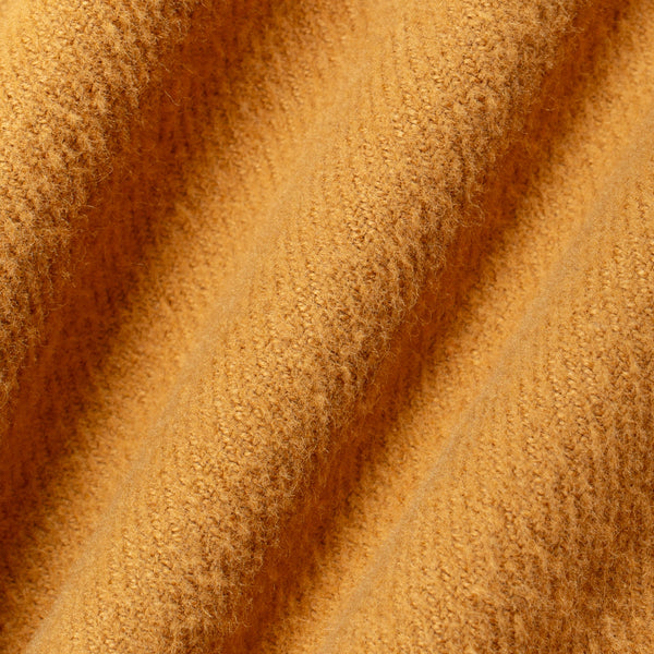 A close-up of textured, fuzzy fabric in a warm mustard yellow or golden ochre color, draped in soft diagonal folds.