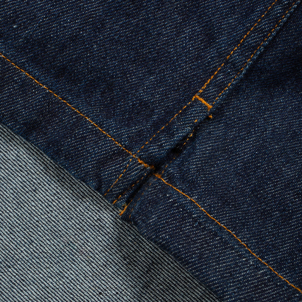 Close-up of dark indigo denim fabric with orange contrast stitching and a lighter gray denim section folded over.
