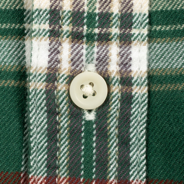 Close-up of a green plaid fabric with white, gray, and red stripes, featuring a single cream-colored button on the placket.