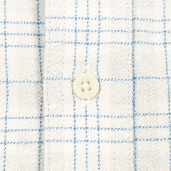 Close-up of a white or off-white fabric with a light blue windowpane plaid pattern and a single cream-colored button at the center.