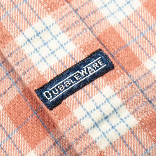 Close-up of a peach and white plaid fabric with a navy blue Dubbleware brand label sewn onto the side.