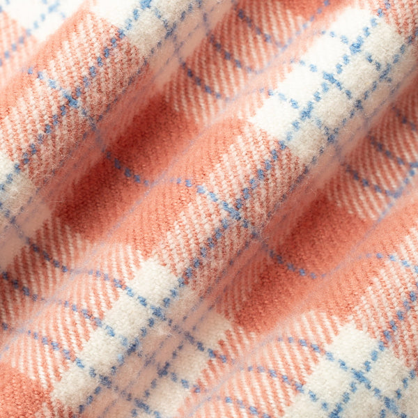 A close-up of a soft, plush fabric with a plaid pattern in peach, cream, and light blue.
