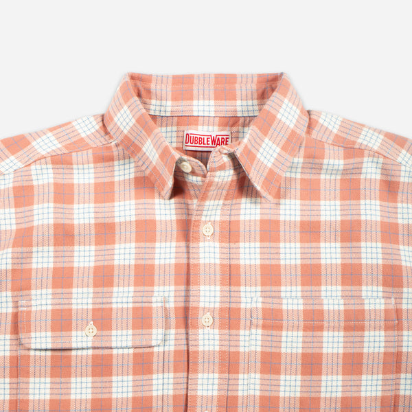 A close-up of a Doubleware button-down shirt featuring a peach-orange and white plaid pattern, with a visible brand label inside the collar.
