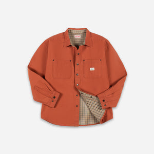 Dubbleware - Dubbleware Lined Snap Overshirt - Dusty Brick Canvas - An orange long-sleeve button-up shirt jacket with two chest pockets, shown flat on a light gray background. The shirt jacket is slightly open to reveal a beige and brown plaid lining. - Alternative View 1