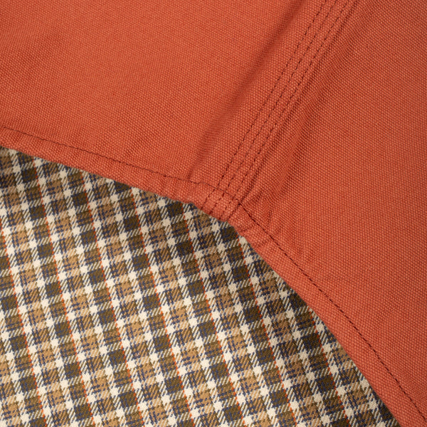 Close-up detail of a garment corner showing a rust-orange woven fabric body meeting a brown, beige, and black plaid lining.