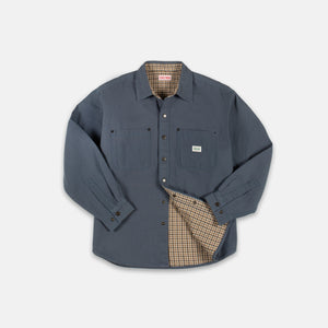 Dubbleware - Dubbleware Lined Snap Overshirt - Indigo Canvas - A slate blue work shirt with a beige and brown checkered lining, shown on a light gray background. The shirt features two chest pockets, a button-down front, and the brand label on the left chest pocket reads 'Fjäl'. - Alternative View 1