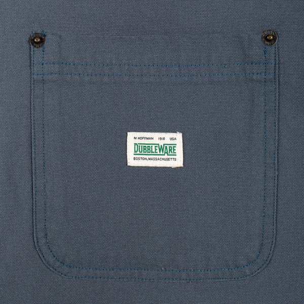 Close-up of a blue canvas work shirt pocket with two metal snap buttons and a white Dubbleware brand label stitched in the center.