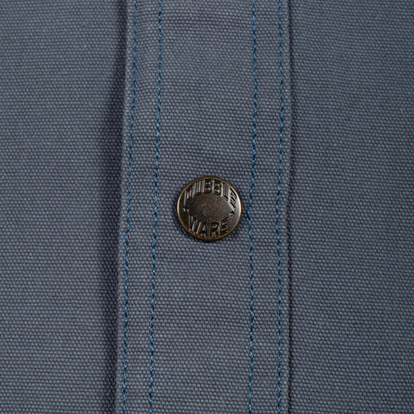 Close-up of a slate blue woven fabric with a single round metal button featuring the 'MURDER WARE' brand name.