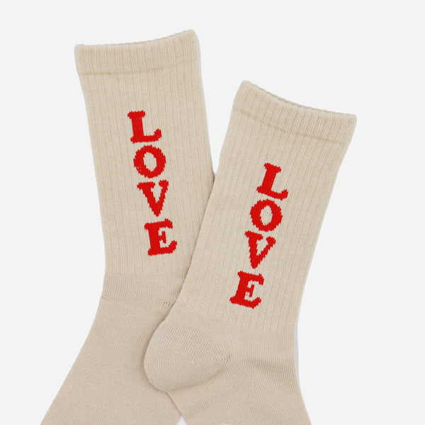 A pair of cream-colored ribbed crew socks with the word 'LOVE' knitted vertically in red on each sock, displayed against a light gray background.