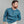 Load image into Gallery viewer, A man wearing a teal blue ribbed long-sleeve henley shirt and off-white jeans, standing against a plain gray studio background.
