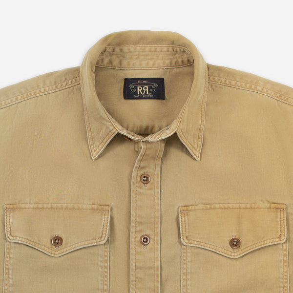 A close-up of a tan cotton button-up shirt with two chest flap pockets and a black collar label reading 'R.A.
