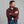 Load image into Gallery viewer, A man wearing a red and yellow plaid flannel shirt over a white t-shirt and blue jeans, standing with arms crossed against a plain gray background.
