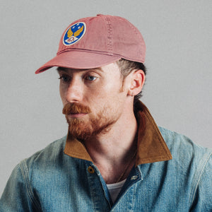 Double RL By Ralph Lauren - Vintage Ball Cap - Faded Red - A man with a red beard wearing a dusty rose baseball cap with a circular blue, yellow, and white logo patch, paired with a blue denim shirt jacket with a brown corduroy collar, set against a plain gray background. - Alternative View 1