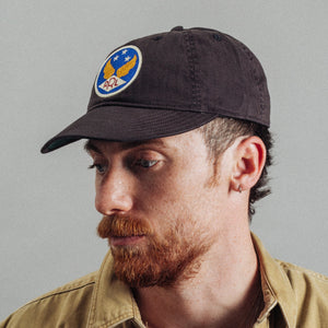 Double RL By Ralph Lauren - Winged Logo Twill Ball Cap - Black - A man wearing a dark brown baseball cap with a circular embroidered patch featuring an eagle and stars, paired with a tan button-up shirt against a plain gray background. - Alternative View 1