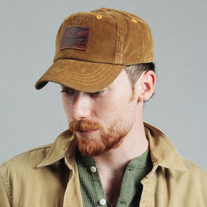 Double RL By Ralph Lauren - RRL Leather Patch Corduroy Trucker Cap Tan - A man wearing a brown corduroy baseball cap with a brown leather patch that reads 'SUNRISE', paired with a tan overshirt and green shirt, against a plain gray background. - Alternative View 1